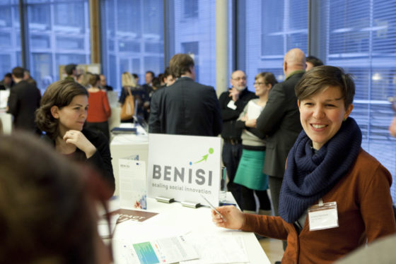 Das Foto zeigt mehrere Infostände, um die je mehrere Personen stehen. Auf dem vordersten Stand sieht man einen Auftseller mit dem Logo von 