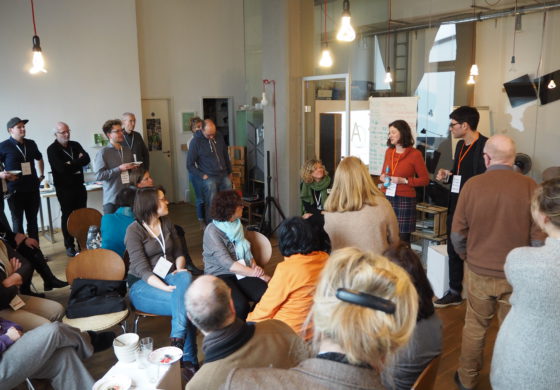 Eine Gruppe von 20 Leuten steht und sitzt um zwei Referenten herum.