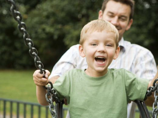 Ein Mann gibt einem Jungen auf einer Schaukel Anschwung.