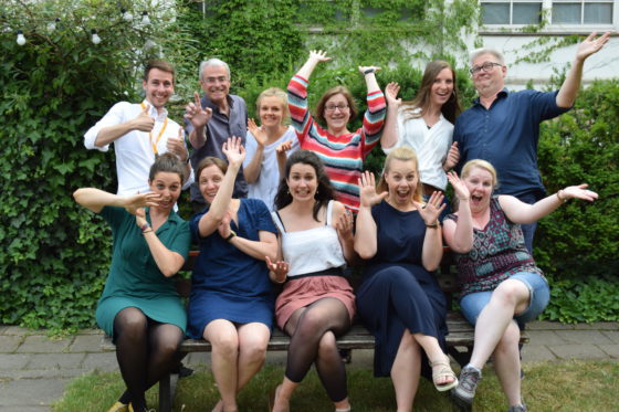 Eine Gruppe junger Männer und Frauen lachen in die Kamera und strecken die Arme hoch.