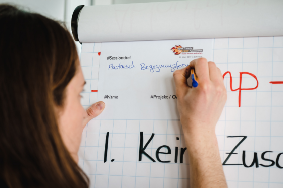 Frau nutzt ein Flipchart als Ablage um etwas auf einen Zettel zu schreiben