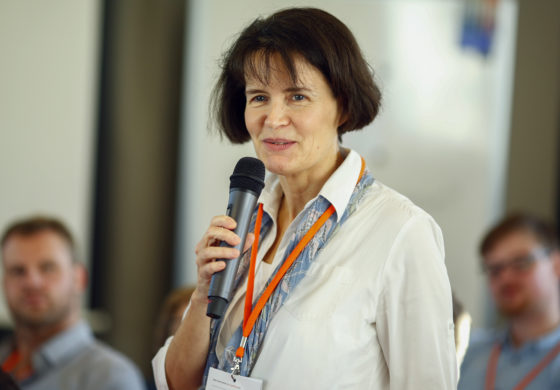 Eine Frau hält ein Mikro in der Hand und spricht vor mehreren Menschen.