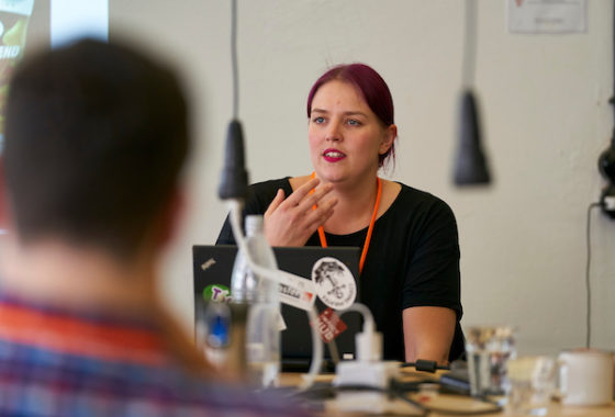 Die Referentin sitzt an einem Tisch und erklärt etwas.