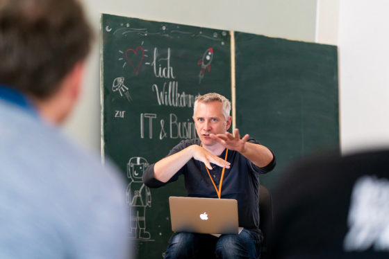 Ein Mann hat einen Laptop auf dem Schoß und gestikuliert.