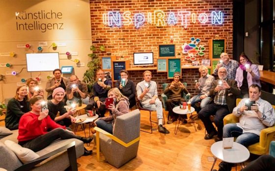 Mehrere Menschen sitzen in einer Runde und halten das Handy in Richtung Kamera.