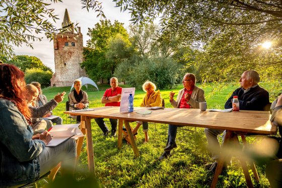 Foto einer Veranstaltung von Vorpommern besser machen: An einem langen Tisch auf einer Wiese unter Obstbäumen sitzen Menschen verschiedenen Alters und diskutieren.