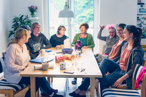 Eine Gruppe Menschen mit und ohne Behinderung sitzt um einen Küchentisch und lacht.