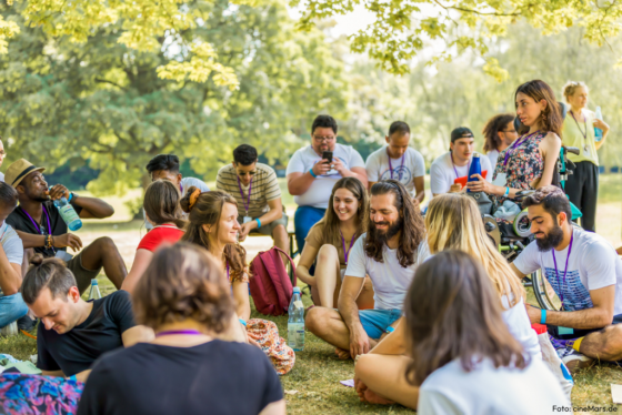 Auf dem Bild sitzen Team-Mitglieder von SwaF in einem Park auf dem Biden. einige haben geschlossene Augen und lächeln.