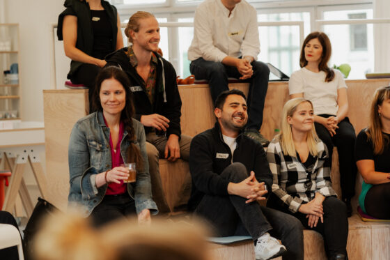 Das Foto zeigt eine Gruppe von Menschen, die auf Holzstufen sitzen. Alle tragen Namensschilder.