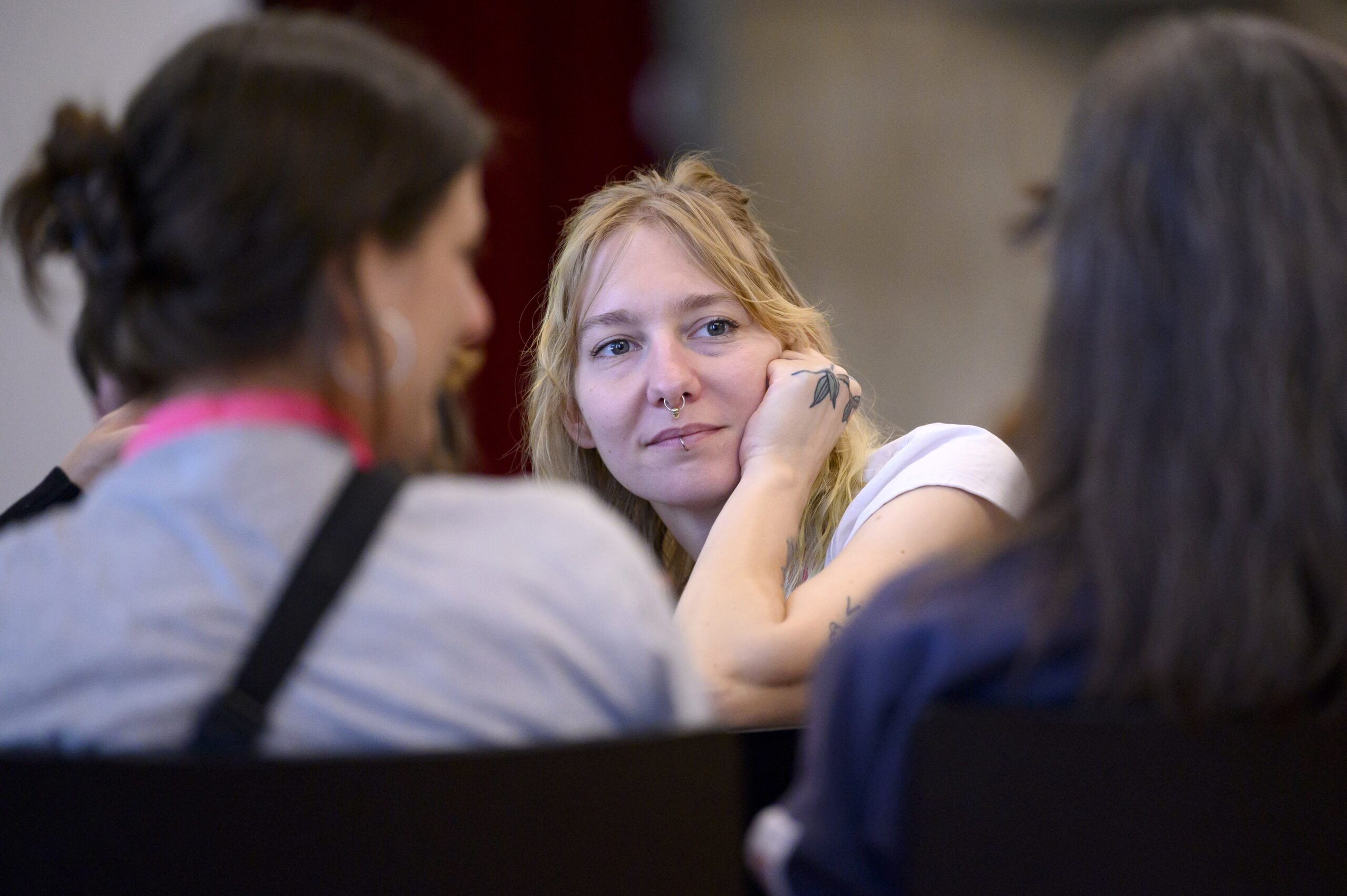 Eine weiblich gelesene Person schaut auf eine Person rechts im Bild, die mit dem Rücken zum Betrachter sitzt